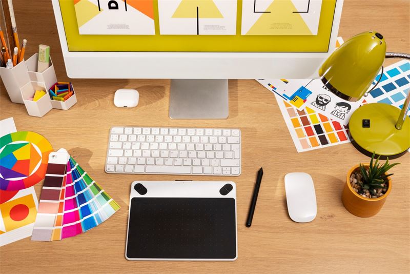 Bureau de graphiste avec nuanciers, tablette graphique et écran affichant des créations